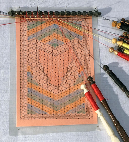 Fox bobbin lace pattern, bobbins, and a wood spindle at the top. 
