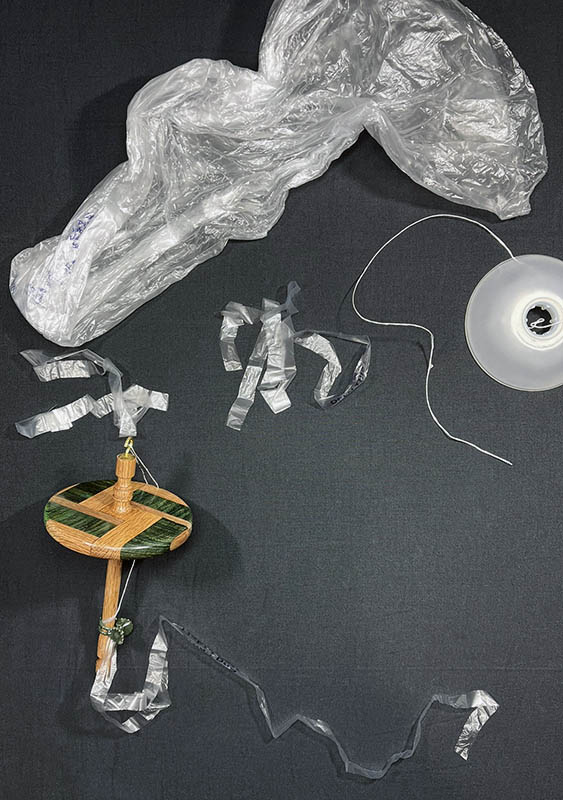 Produce bag, strip of the bag ready to spin, drop spindle, and some finished thread. 