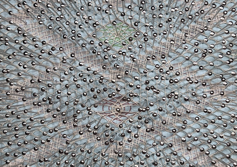 Close-up of lace in progress with visible pins, showing cloth stitch and half stitch spider patterns.