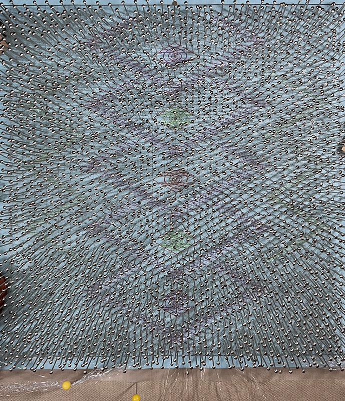 The completed lace piece on the pillow, still pinned in place, viewed in regular light.