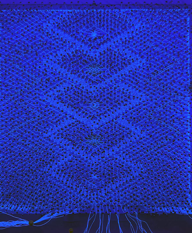 The finished lace glowing under UV light while still held by pins.